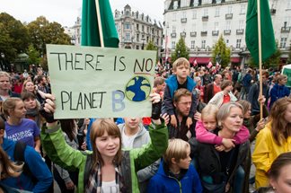 families at a climate change protest event with girl carrying a sign 'there is no planet B'
