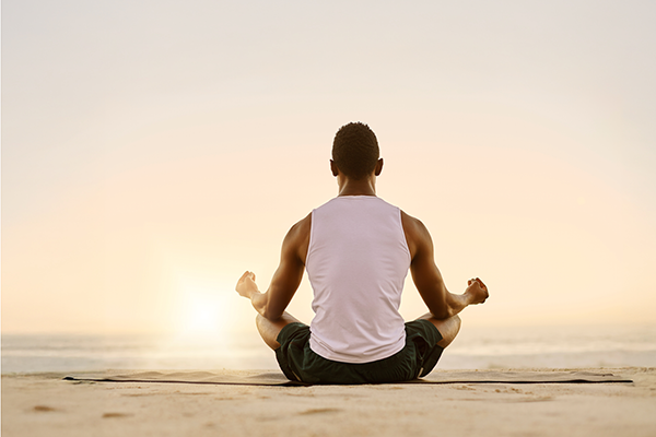 Man meditating on beach during sunrise